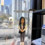 透明展示盒內的客製重案組女警公仔，白襯衫配深灰背心與長褲，胸前佩章與識別證，手提黑色斜背包，立於石紋底座，前有中文銘牌