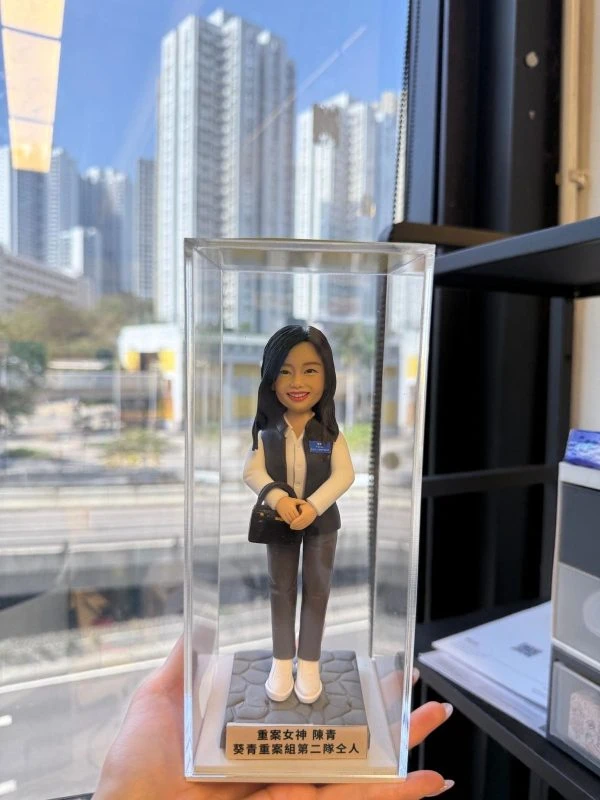 透明展示盒內的客製重案組女警公仔，白襯衫配深灰背心與長褲，胸前佩章與識別證，手提黑色斜背包，立於石紋底座，前有中文銘牌