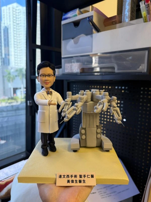 客製外科醫師公仔穿白袍打領結，伸手示意站在手術機器人旁，方形底座前有中英文銘牌